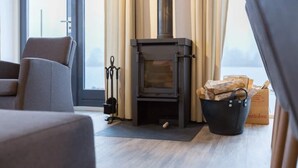 A modern living room with a wood-burning stove, a comfortable sofa, and a view through a large window. - Holiday home in Langelille for family (Langelille)