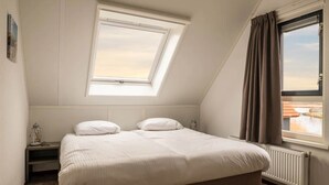 A bedroom with a skylight, a bed, a nightstand, a window with curtains, and a view of buildings outside. - Holiday home in Langelille for family (Langelille)