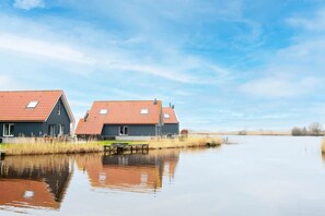 Two modern houses with red roofs and grey walls, situated by a calm water body. - Holiday home in Langelille for family (Langelille)