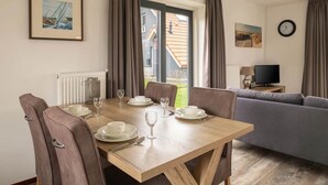 A dining area with a wooden table set for four, a grey sofa, and a TV on a side table. - Holiday home in Langelille for family (Langelille)