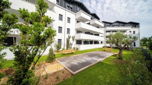 Un moderno edificio residencial de varios pisos con balcones, un patio empedrado y zonas verdes circundantes.