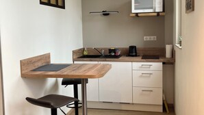 Uma cozinha compacta com micro-ondas, uma pia pequena e uma mesa de madeira com uma cadeira.