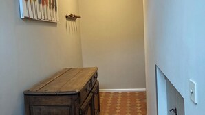 Um corredor estreito com um armário de madeira, um quadro abstrato na parede e chão de azulejos.