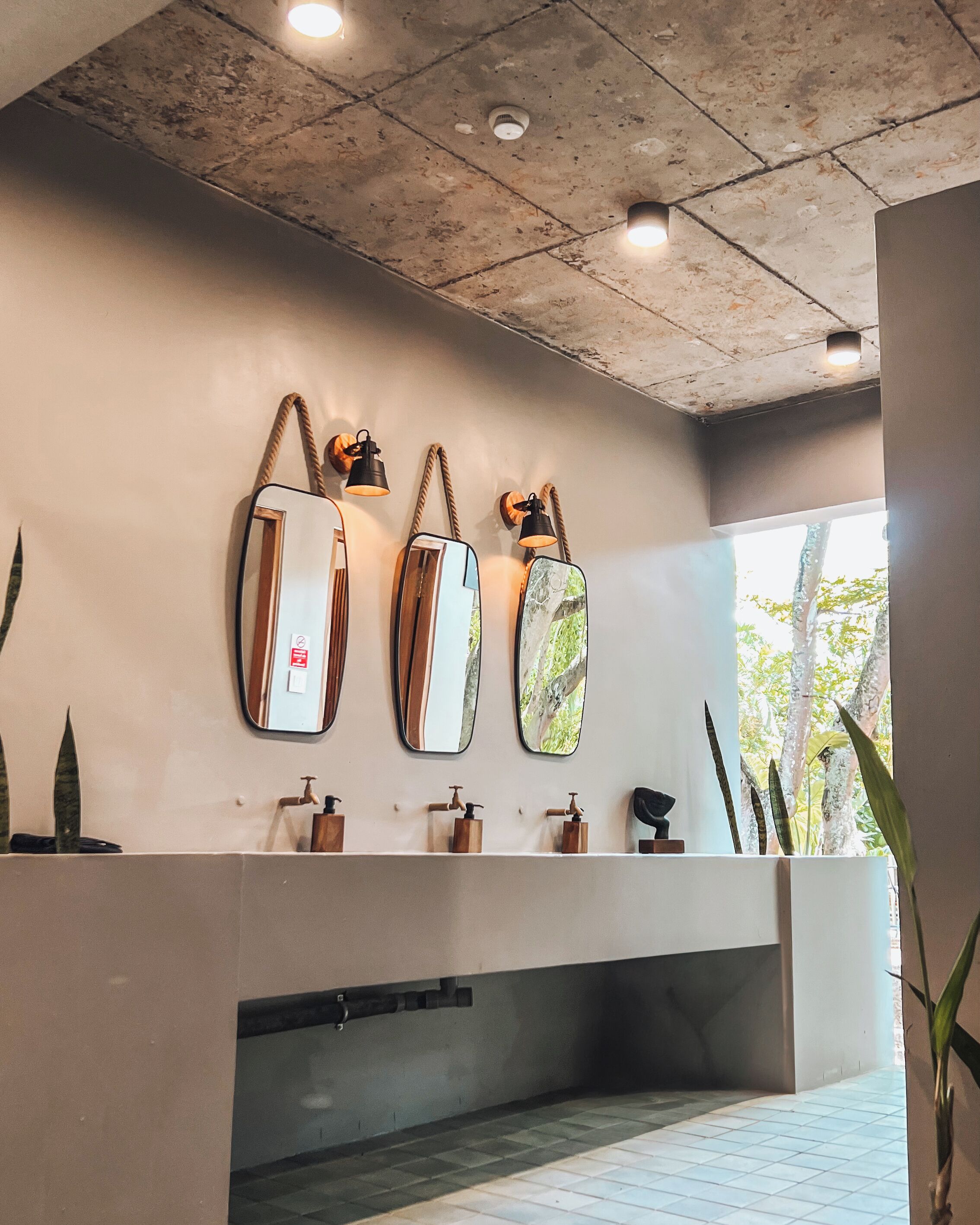 Een badkamer met drie spiegels, een wastafel met zeepdispensers en een plafond met inbouwverlichting.