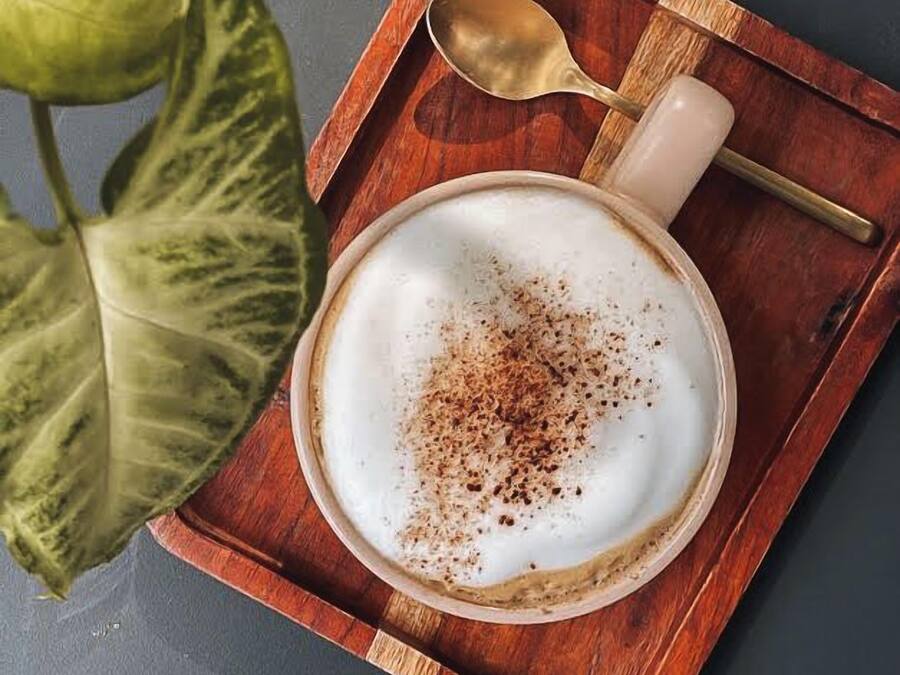 A cup of coffee with a spoon on a wooden tray.