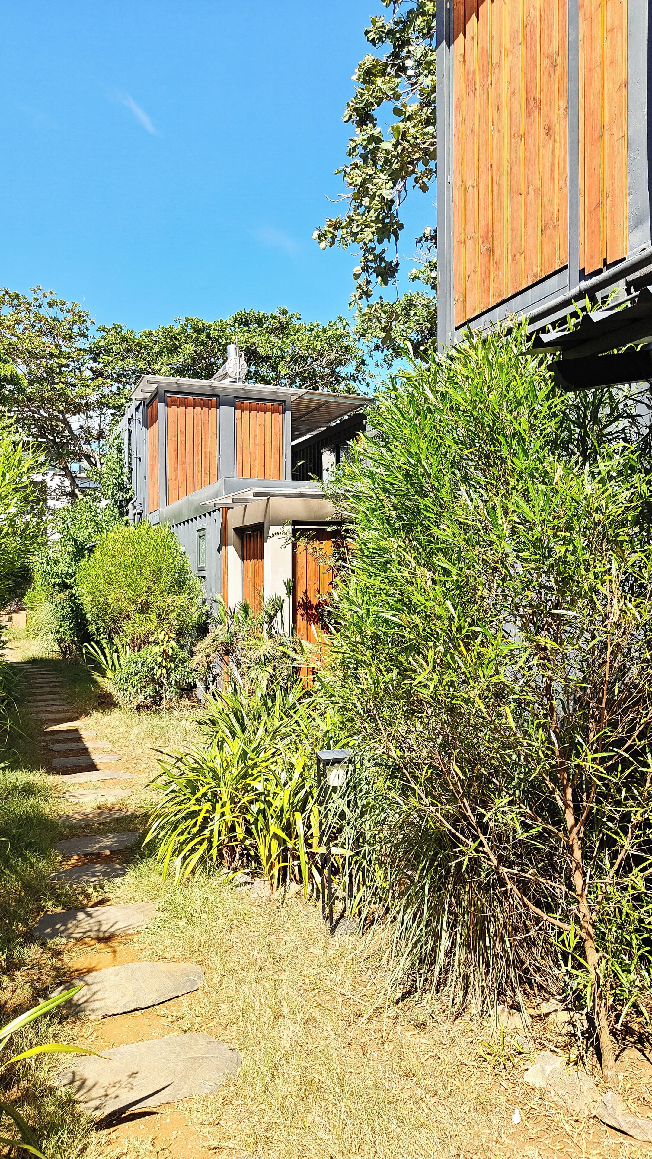 Un bâtiment moderne doté d’une façade en bois, d’un chemin en pierre et d’une végétation luxuriante.