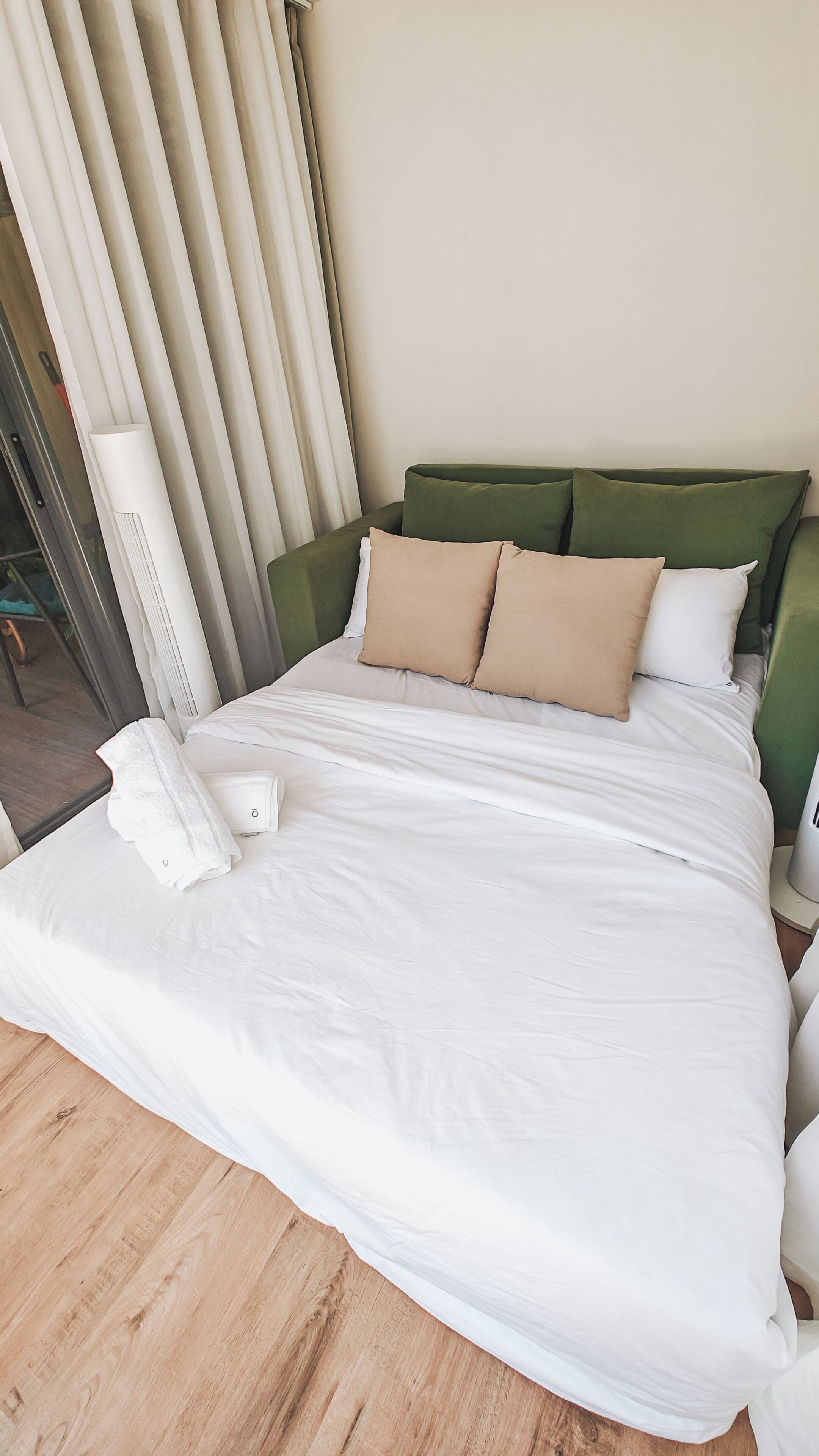 A neatly made bed with white linens, a green headboard, and beige pillows.