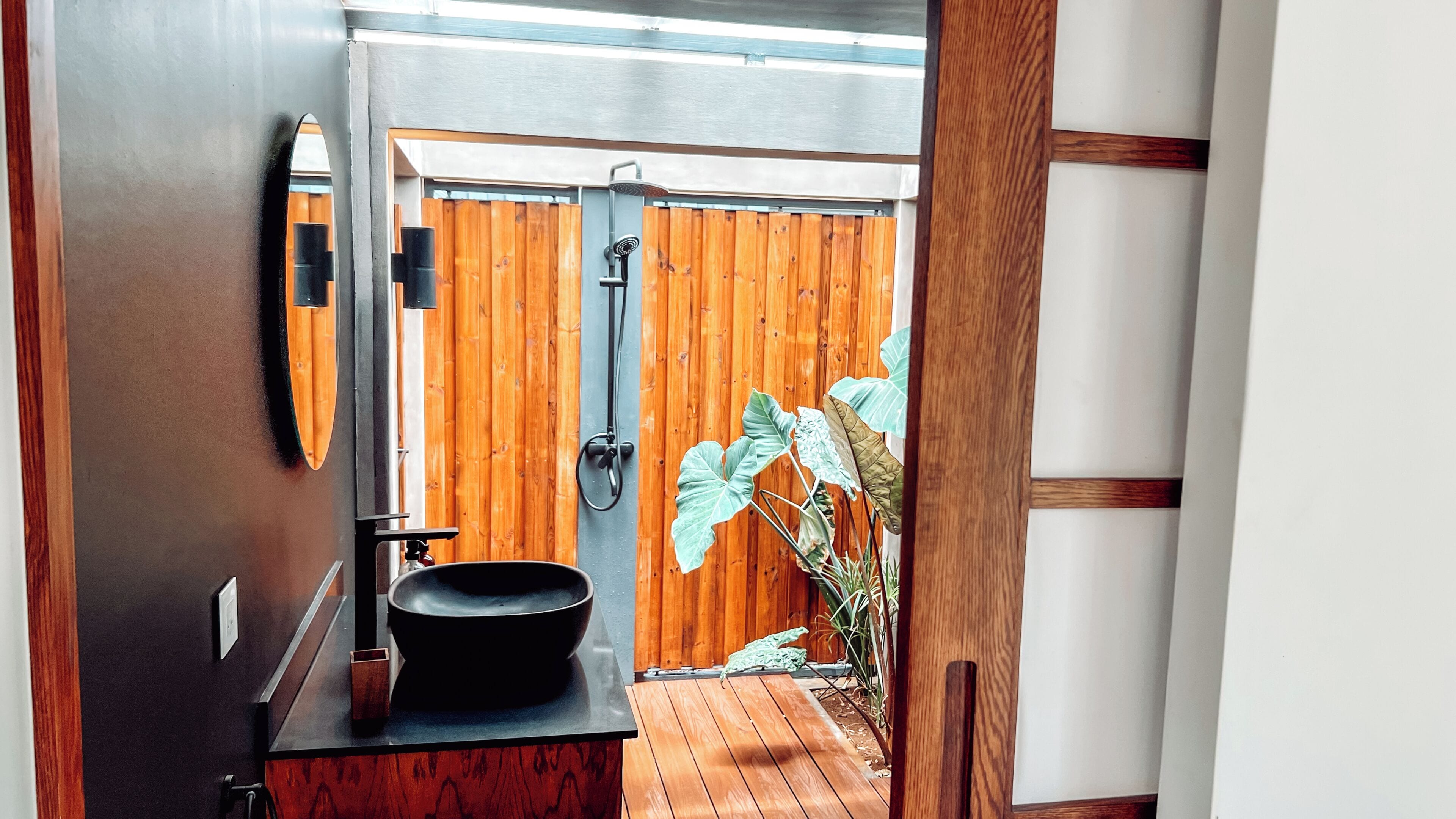 A bathroom with a black sink, wooden door, and a shower area.