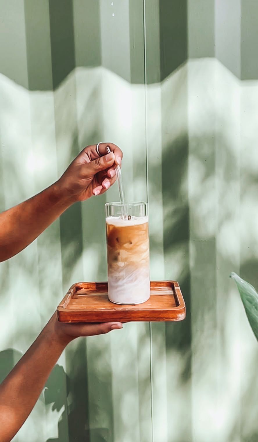 A hand holding a glass with a layered drink, placed on a wooden tray.