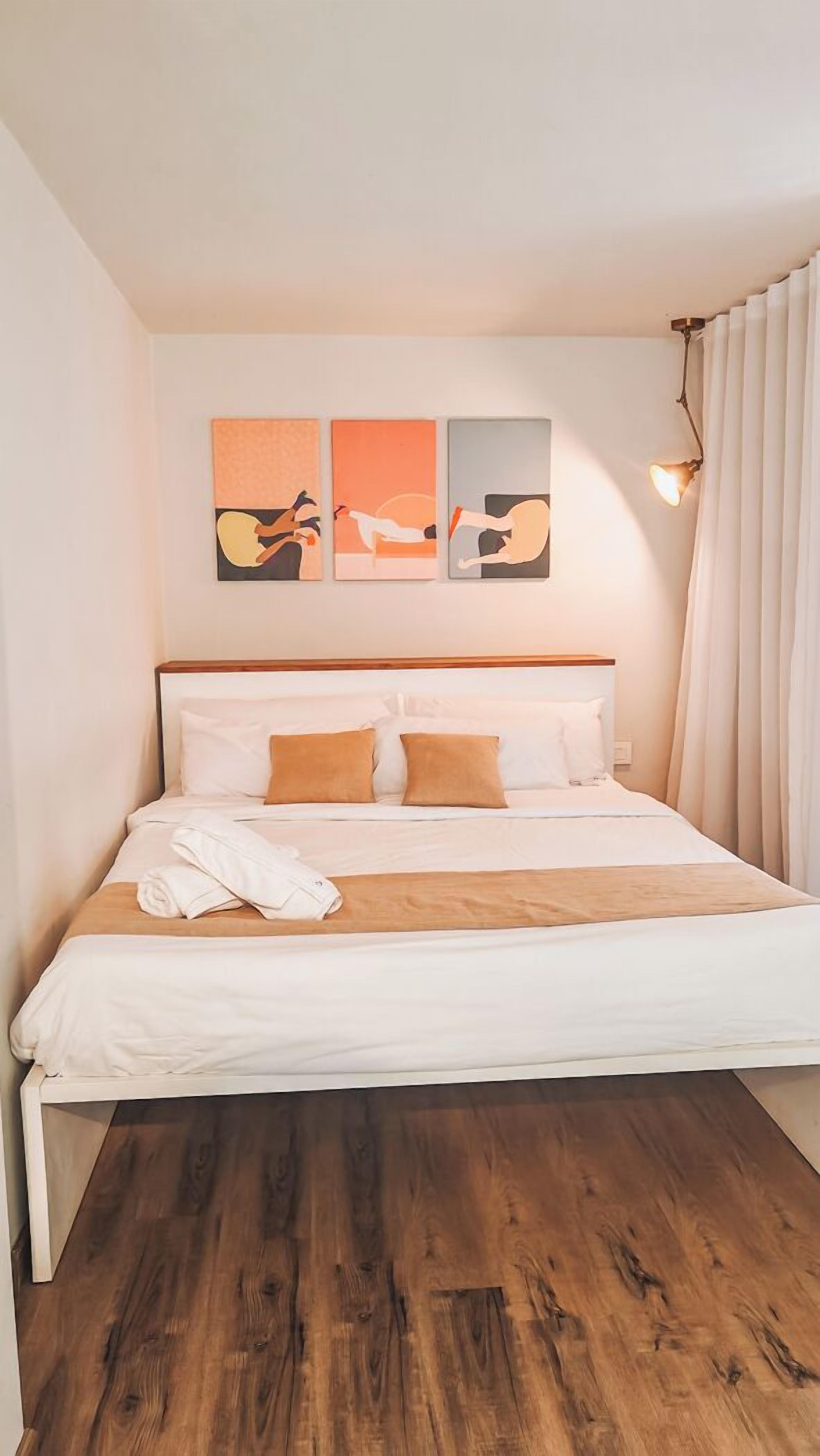 Ein Hotelzimmer mit Bett, Holzboden und einer Wand mit drei Kunstwerken.