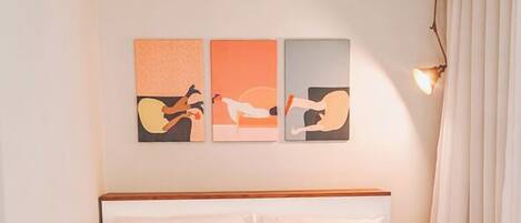 A hotel room with a bed, wooden flooring, and a wall with three artwork pieces.