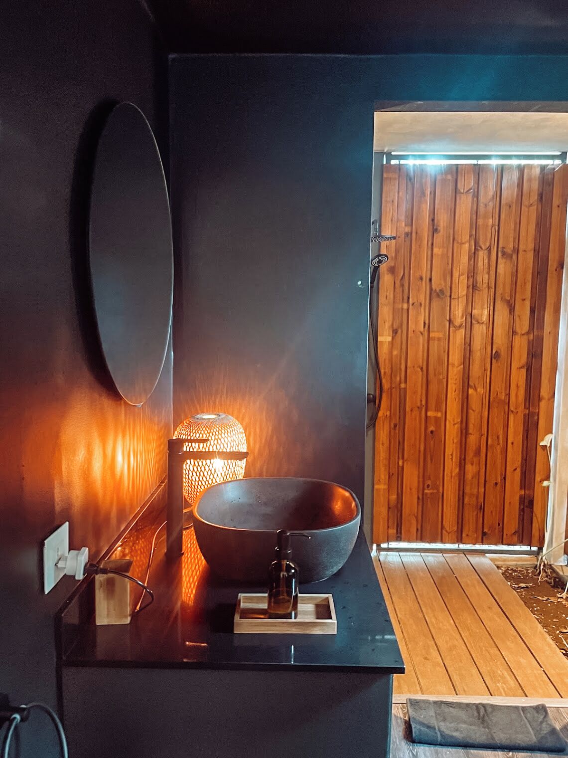Un baño moderno con un espejo grande, un lavabo negro y una lámpara de pared con textura.