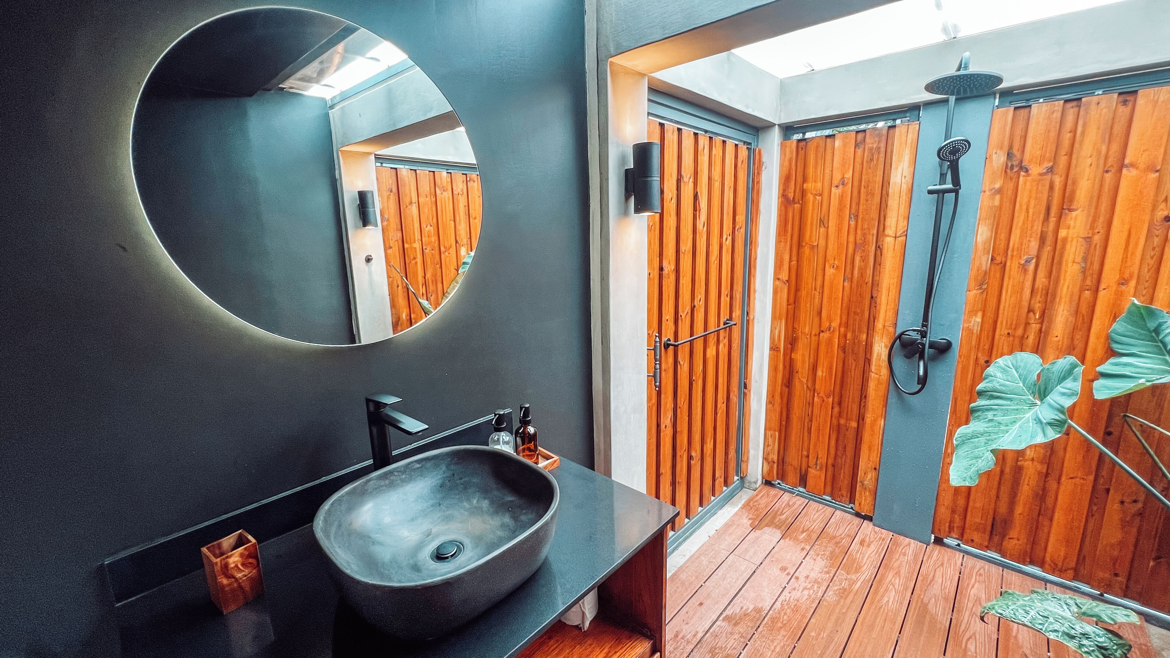 Un baño moderno con un espejo redondo, un lavabo negro, puertas de madera y una ducha.