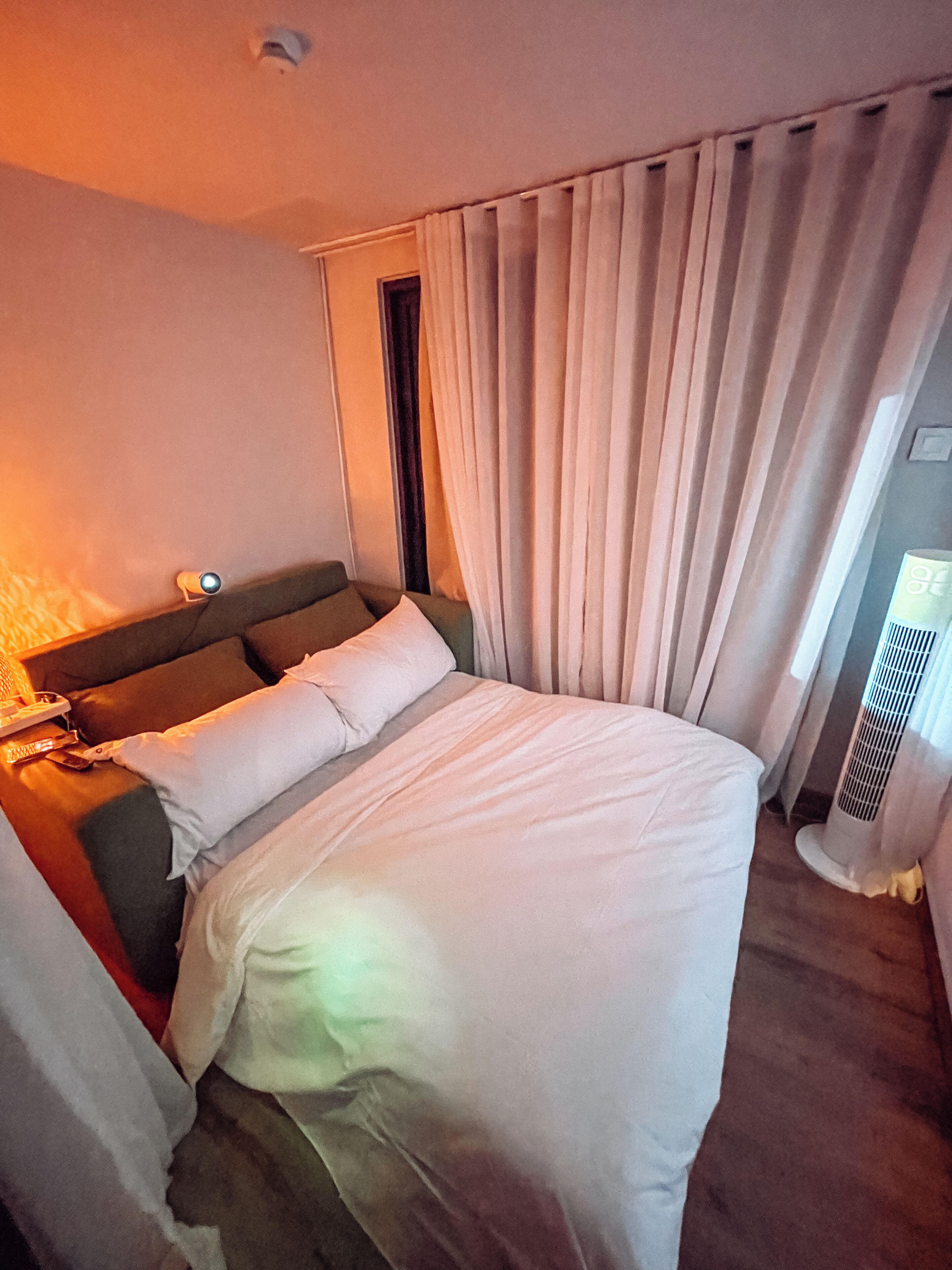 Una habitación de hotel con cama, cortinas, ventana y una lámpara fijada a la pared.