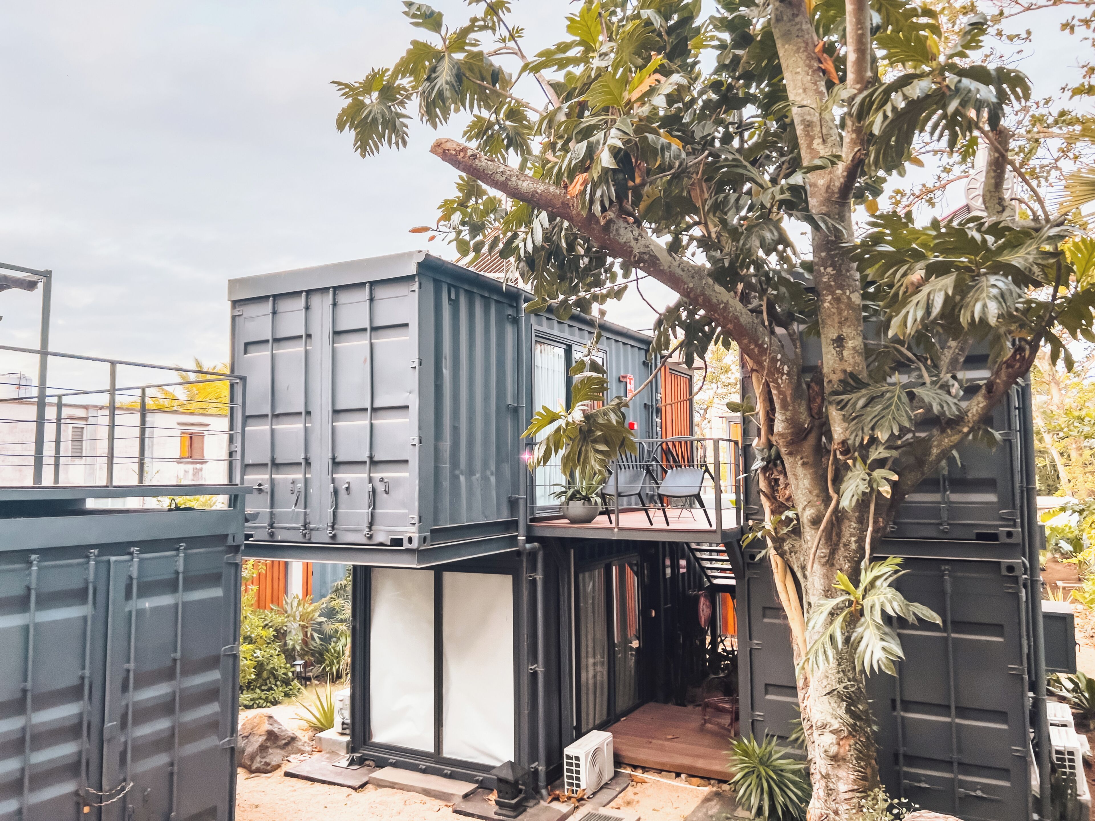 A modular building with a balcony, a potted plant, and a small outdoor seating area.
