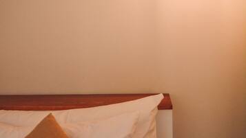 Un lit avec une literie blanche et un oreiller marron, une tête de lit en bois et un luminaire suspendu.