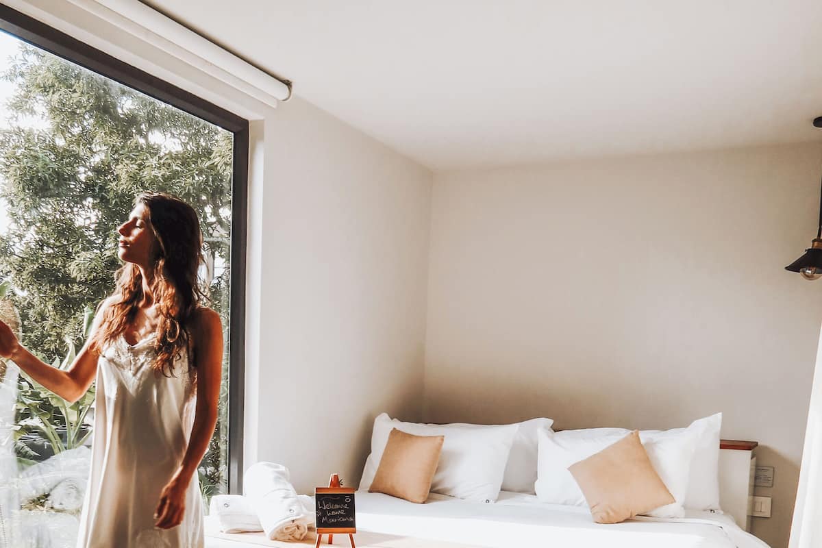 A bedroom with a bed, pillows, a small table, and a window.