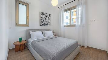 Un dormitorio moderno con una cama grande, una mesita de noche, una lámpara de pared y un ventanal con cortinas.