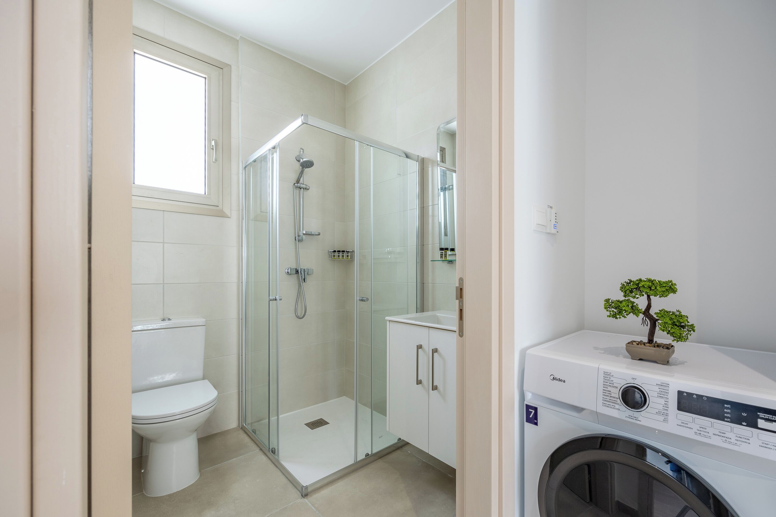 A modern bathroom with a glass-enclosed shower, a toilet, and a washing machine.