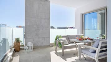 Un balcón moderno con sofá, sillas y mesa de comedor, con vistas a la ciudad.
