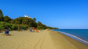 A sandy beach with a playground and a white building on a hill. - Mulberry Court Premium Apartments (Limassol)