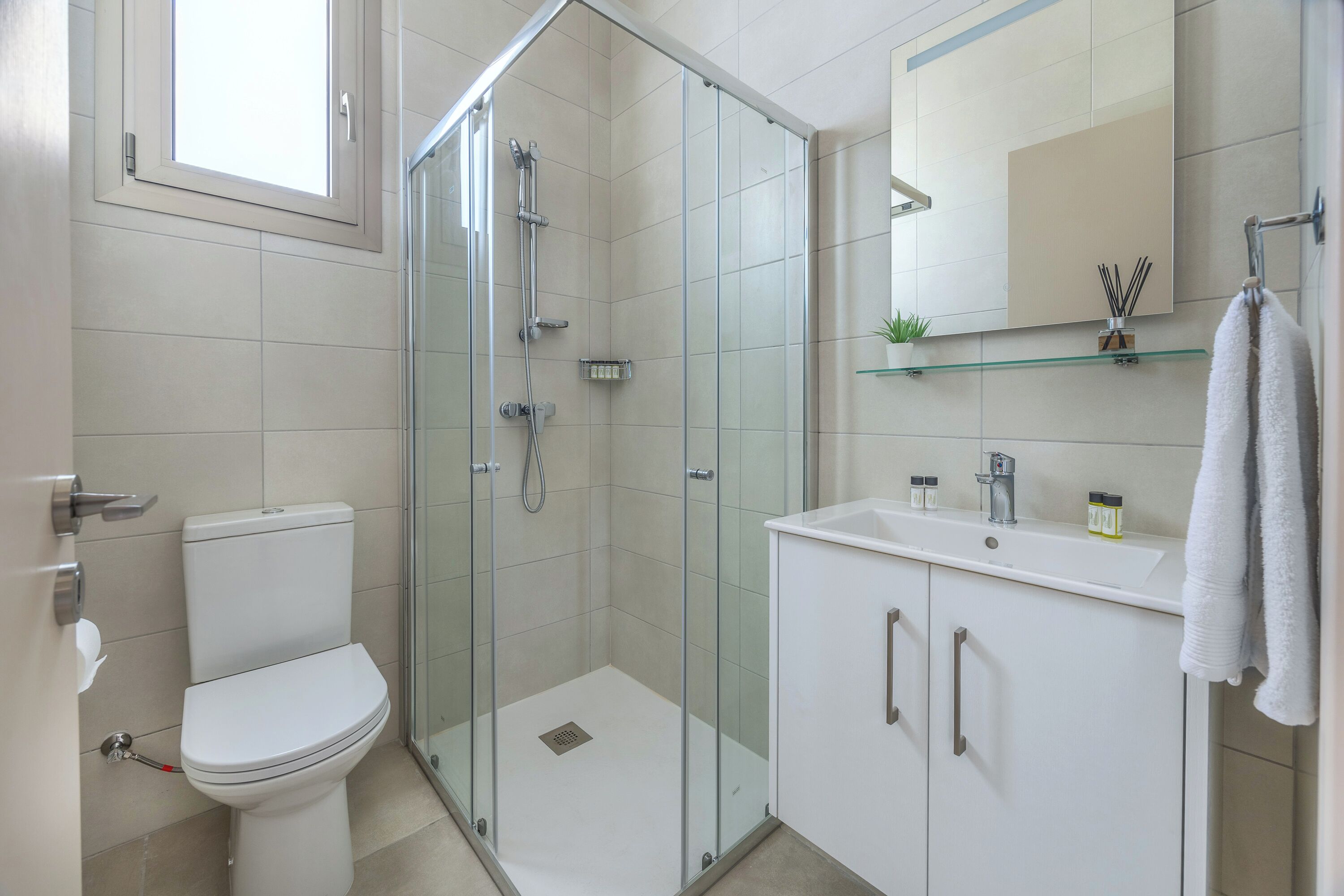 Une salle de bain moderne avec une douche à parois de verre, des toilettes, un lavabo avec un miroir au-dessus et une serviette accrochée au mur.