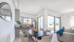 A modern apartment with a dining area, kitchen, and balcony with city views. - Mulberry Court Premium Apartments (Limassol)