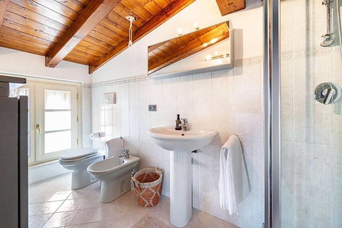 A bathroom with a wooden ceiling, a pedestal sink, a bidet, and a glass shower enclosure.