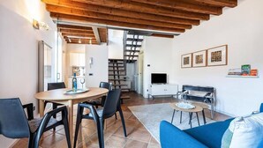 Een moderne woonkamer met een houten plafond, een blauwe bank, een eettafel met stoelen en een televisie op een wit dressoir.