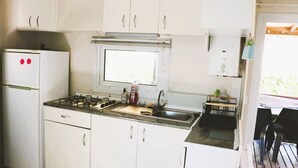 A compact kitchen with white cabinets, a gas stove, a sink, and a window above the countertop. - Air-conditioned mobile home, 5-minute walk from Lac de Biscarrosse "Menthe à l'eau" lake (Biscarrosse)