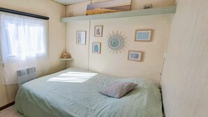 A bedroom with a bed, a window with curtains, and wall-mounted decorations. - Air-conditioned mobile home, 5-minute walk from Lac de Biscarrosse "Menthe à l'eau" lake (Biscarrosse)