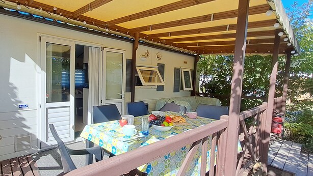 A covered outdoor area with a table set for breakfast, a wooden deck, and a white RV with blue shutters. - Air-conditioned mobile home, 5-minute walk from Lac de Biscarrosse "Menthe à l'eau" lake (Biscarrosse)