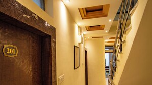 Un couloir d’hôtel avec une porte en bois portant le numéro « 201 », un sol en marbre et un escalier avec des rampes en métal.