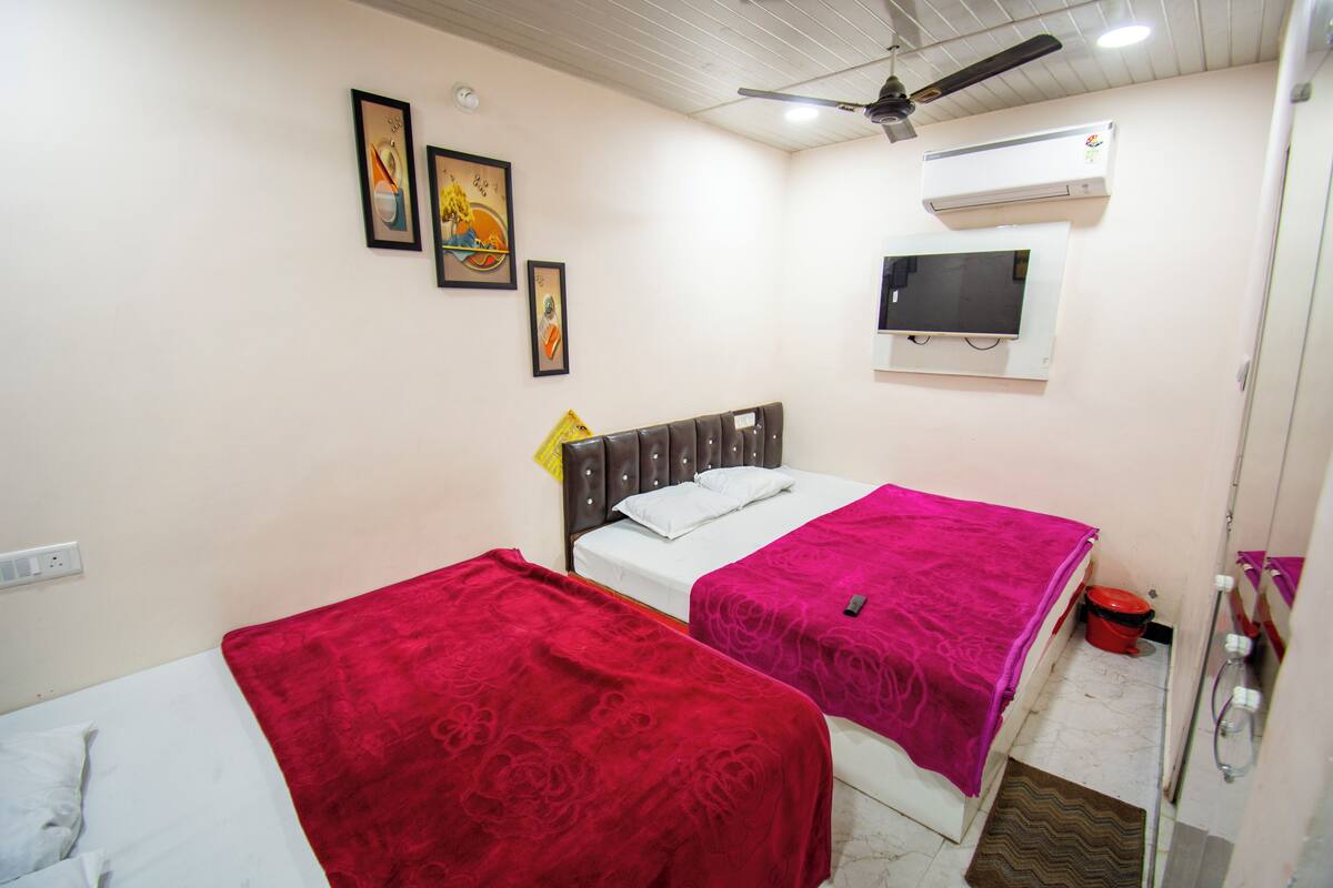 A bedroom with two beds, a ceiling fan, an air conditioner, a TV, and framed artwork on the wall.