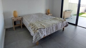 Un dormitorio moderno con una cama grande, dos mesitas de noche, una lámpara de techo tejida y un ventanal corredero que da a un balcón.
