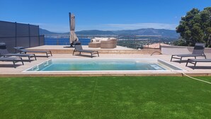 Zona de piscina en la azotea con vistas al mar y a las montañas, sillas de descanso y una mesa cubierta.
