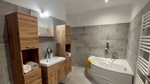 Un baño moderno con dos lavamanos, una bañera grande, muebles de madera y paredes revestidas de cerámica gris.