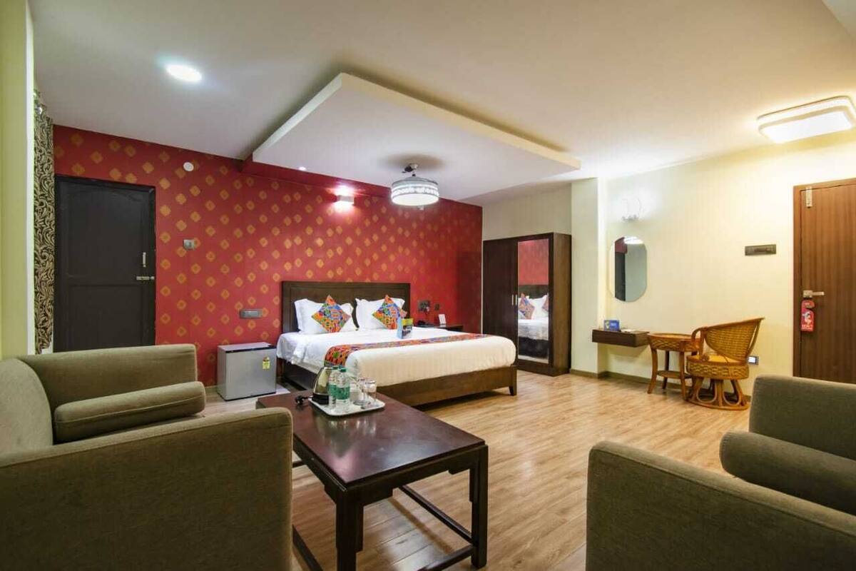 A hotel room with a bed, a desk, two chairs, and a small table with items on it.