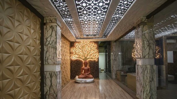 A hallway with a central Buddha statue, marble walls, and a patterned ceiling. - Prince Park Vellore (Vellore)