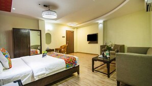 A hotel room with a bed, a sofa, a TV, and a small table with a vase. - Prince Park Vellore (Vellore)