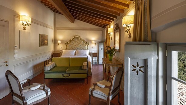 A hotel room with a bed, a green sofa, two chairs, a small table, and a decorative mirror.