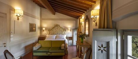 Habitación de hotel con una cama, un sofá verde, dos sillas, una mesita y un espejo decorativo.