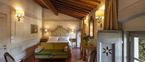 A hotel room with a bed, a green sofa, two chairs, a small table, and a decorative mirror.