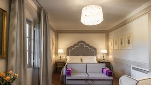 A hotel room with a bed, a sofa, a nightstand, a lamp, and a chandelier.