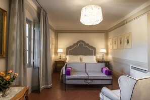 Une chambre d’hôtel comprenant un lit, un canapé, une table de chevet, une lampe et un lustre.