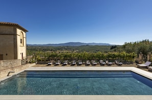 A swimming pool with lounge chairs and a view of vineyards and mountains.