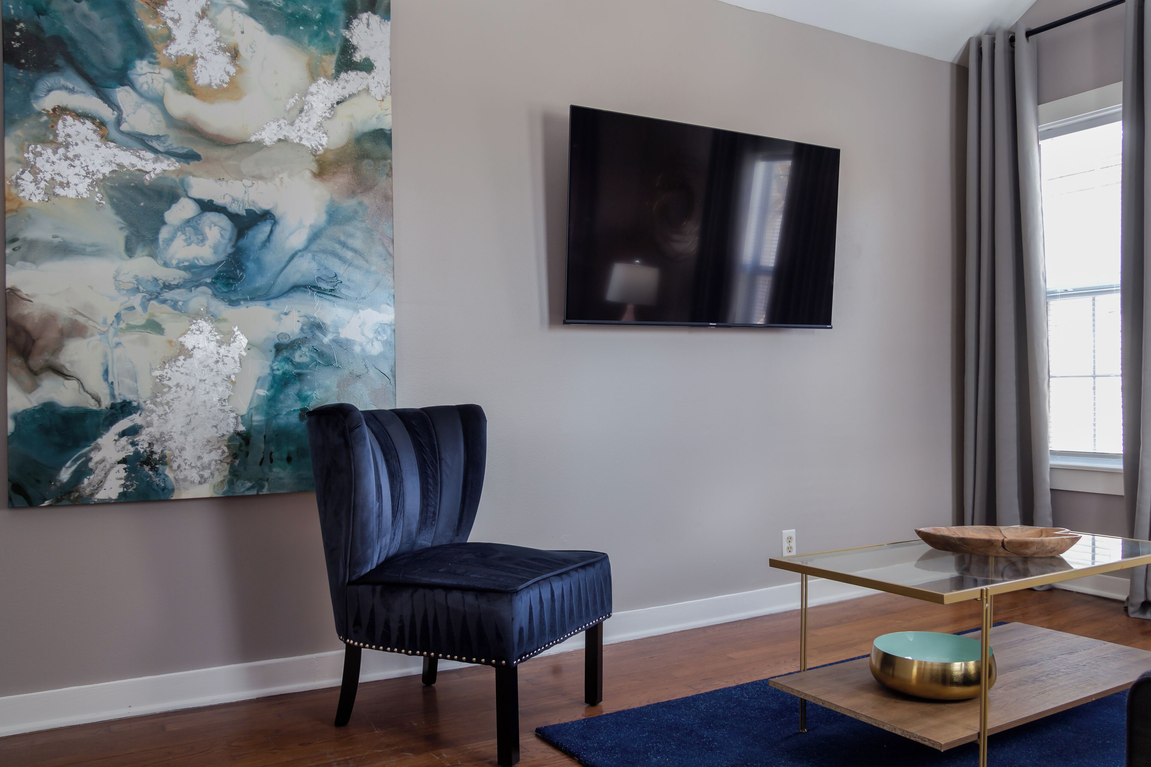 Een moderne woonkamer met een donkerblauwe fauteuil, een salontafel met glazen blad en een groot abstract schilderij aan de muur.