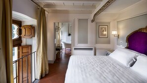 Habitación de hotel con una cama grande, cabecera de madera, baño con bañera y balcón con barandilla.
