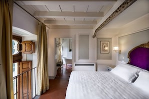 Une chambre d’hôtel avec un grand lit, une tête de lit en bois, une salle de bain avec baignoire et un balcon doté d’une rambarde.