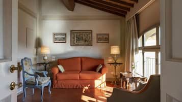 Ein Wohnzimmer mit einer Couch, einem Sessel und zwei Lampen. An der Wand hängen drei gerahmte Bilder.
